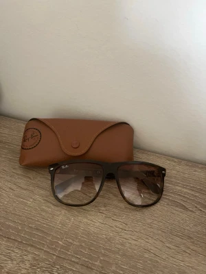 Ray-Ban Boyfriend - Snygga svarta solglasögon från Ray-Ban med klassisk fyrkantig form och bruna tonade glas. Kommer med ett brunt fodral i skinn-look. Perfekta för att lyfta din stil i solen.