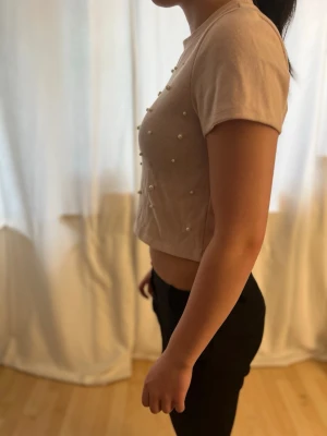 Rosa T-shirt med pärlor  - En jätte söt rosa T-shirt i hyfsat tjockt material. Har pärlor på hela framsidan, men inga bak på ryggen. Perfekt att styla med ett linne under. Hör av dig vid fler frågor 