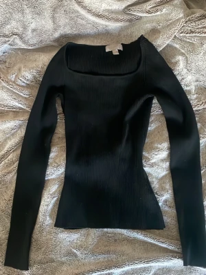 Svart ribbad topp från H&M - Säljer en svart, ribbad långärmad topp från H&M i storlek XS. Toppen har en fyrkantig ringning och är figurnära med stretchigt material. Perfekt att styla med jeans eller kjol för en clean look.