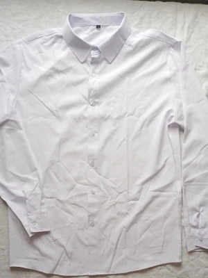 Klassisk vit skjorta med knappar - Stilren vit skjorta med lång ärm och klassisk krage. Skjortan har knäppning framtill och är tillverkad i ett mjukt bomullstyg. Perfekt för en clean och enkel look.