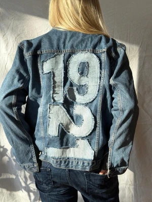 Jeansjacka med 1921-tryck - Jeansjacka med stora siffror '1992' i ljus denim på ryggen. Perfekt för dig som vill sticka ut med en unik detalj.🩵