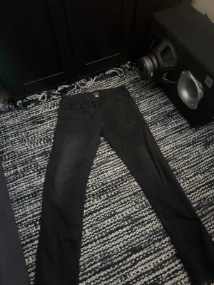 Svarta true religion Jean - Snygga svarta slim fit jeans med klassisk femficksdesign och knappgylf. Jeansen har raka ben och är tillverkade i ett mjukt bomullsmaterial med lite stretch för extra komfort. Passar perfekt till en avslappnad streetwear-look.