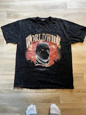 Svart Worldwide t-shirt Boohooman - Cool svart t-shirt från Boohooman med stort tryck 'WORLDWIDE' och motiv av en rånarluva på framsidan. T-shirten har korta ärmar, rund hals och en tvättad vintage-look. Perfekt för dig som gillar streetwear och statement-plagg.