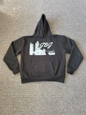 Hoodie - Helt ny, nypris 799kr. Säljer en svart hoodie med stor vit stadssilhuett och JBJ-tryck på bröstet. Hoodien har klassisk känguruficka framtill och en rymlig huva. Perfekt för dig som gillar streetwear och vill ha en unik look.