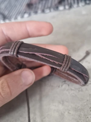 Brunt läderarmband med snördetaljer - Snyggt armband i mörkbrunt läder med tvinnade snördetaljer. Justerbar storlek med knytband för perfekt passform. Armbandet har en enkel men cool design som passar till många olika stilar.