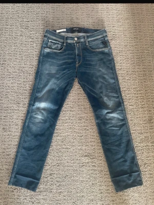 Blå Replay jeans med raka ben - Säljer ett par blå jeans från Replay med raka ben och klassisk femficksmodell. Jeansen har snygga slitningar och kontrastsömmar som ger en cool look. Perfekta för dig som gillar en avslappnad men ändå stilren stil.