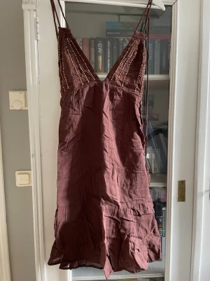 Brun kort klänning med snörning - Kort brun klänning med tunna axelband och djup v-ringning. Sparsamt använd och mycket bra skick, perfekt för sommaren och semestern. 