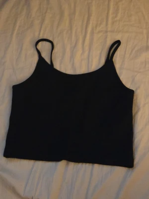 Svart croppad linnetopp - En enkel och stilren svart croppad linnetopp med smala axelband. Perfekt att matcha med höga jeans eller kjol för en trendig look. Tunn och lätt, passar bra till varma dagar.