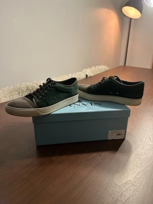 Gröna  Lanvin - Stilrena gröna sneakers från Lanvin med ovandel i mocka och tåparti i grått läder. Skorna har vita sulor och svarta skosnören. Perfekta för dig som gillar en clean och exklusiv look med en twist av premiumkänsla. Tecken på användning men fortfarande i bra skick och kommer kunna användas ett bra bra tag till.