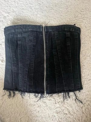 Svart denimkorsett med dragkedja - Säljer en svart korsett i denim med dragkedja framtill och smock baktill.