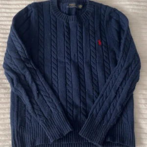  Polo Ralph Lauren tröja  - Kabelstickad mörkblå tröja från Polo Ralph Lauren med klassisk rund halsringning och röd broderad logga på bröstet. Tröjan är långärmad och har breda ribbade muddar vid ärmslut och nederkant. Lite noppig men annars inga defekter, pris kan diskuteras! Bara att dm:a vid frågor eller funderingar!💕