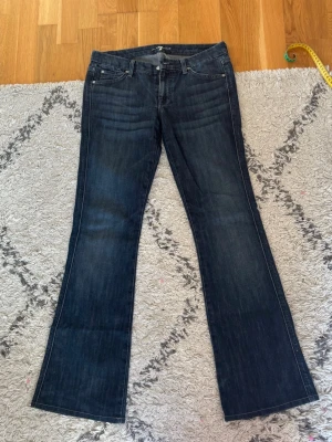 Mörkblå bootcut jeans från 7 For All Mankind - Snygga mörkblå bootcut jeans från 7 For All Mankind med klassisk femficksmodell och diskreta slitningar. Jeansen har broderade bakfickor med A-logga och är tillverkade i mjuk denim med lite stretch för extra komfort.