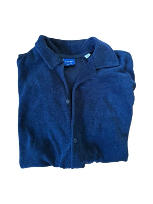 Mörkblå kortärmad frotte skjorta Jack & Jones - Snygg mörkblå skjorta från Jack & Jones i mjukt material. Skjortan har korta ärmar, klassisk krage och knappar framtill. Perfekt till jeans eller chinos för en avslappnad look.