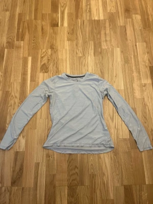 Ljusblå långärmad träningströja SOC - Grå långärmad träningströja från SOC med rund hals och meshpanel på insidan för extra ventilation. Tillverkad i ett lätt och snabbtorkande funktionsmaterial som passar perfekt till träning och sportaktiviteter.