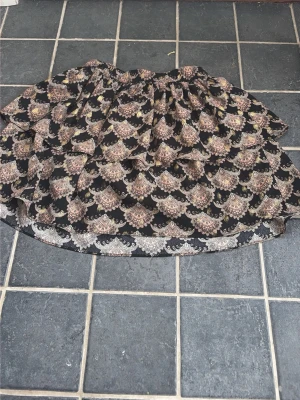 Mönstrad kortkjol från Petit Sofie Schnoor - Kortkjol från Petit Sofie Schnoor med ett unikt mönster i svart, beige och guld. Kjolen har volangdetaljer och elastisk midja för en bekväm passform. Perfekt för dig som gillar statement-plagg med snygga detaljer.