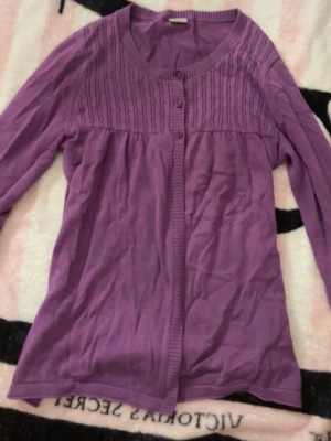 Lila kofta med ribbad detalj - Lila kofta med rund halsringning och ribbade detaljer upptill. Koftan har långa ärmar och knäpps framtill med tre knappar. Perfekt för lager på lager och enkel att matcha med olika outfits.