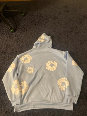 Denim tears hoodie  - Säljer en ljusblå hoodie med vita blommönster över hela tröjan. Hoodien har en klassisk huva och en stor magficka framtill. Mjuk och skön passform, perfekt för chill dagar. Hör av er vid frågor eller funderingar 