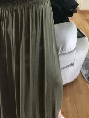 Olivgrön långkjol med resårmidja - Säljer en olivgrön långkjol med bred resår i midjan. Kjolen har ett mjukt, tunt tyg som faller snyggt och ger en avslappnad look. Perfekt att styla med sneakers eller sandaler för en chill vibe.