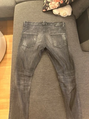 Grå slitna jeans från Dsquared2 - Säljer ett par grå jeans från Dsquared2 med slitningar och hål på framsidan för en cool, trendig look. Jeansen har fem fickor, smal passform och detaljerade sömmar. Perfekta för dig som gillar streetstyle och vill sticka ut.