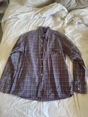 Rutig skjorta från Gant storlek L - Klassisk rutig skjorta från Gant i bomull med blå, röda och gröna toner. Skjortan har lång ärm, knappar framtill och button-down krage. Perfekt för en avslappnad men ändå stilren look.