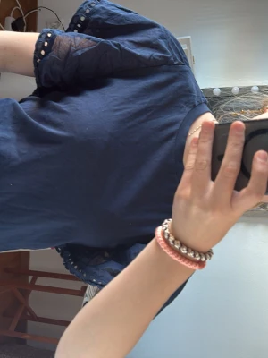 Mörkblå topp med puffiga armar - Snygg mörkblå topp med korta puffärmar och spetsdetaljer längs ärmarna. Rund halsringning och mjukt bomullsmaterial som känns skönt mot huden. Perfekt för dig som vill ha en enkel men ändå unik topp med fina detaljer.