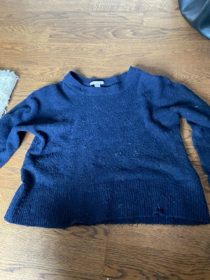 Mörkblå stickad tröja - Mysig mörkblå stickad tröja med rund halsringning och bred ribbad kant nedtill. Tröjan har långa ärmar och en avslappnad passform, perfekt för kyliga dagar. Materialet känns mjukt och bekvämt mot huden. Har blivit ganska nåpprig!