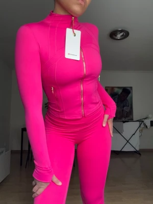 Rosa träningsset från Lululemon - Säljer ett snyggt och figurnära träningsset från Lululemon i stark rosa färg.🩷Setet består av en långärmad zip-jacka med hög krage och guldiga dragkedjor samt matchande tights.🩷Materialet är stretchigt och följsamt, perfekt för gymmet eller yoga🩷.                                                             ‼️OBS‼️- Jag har i både storlek 6 & 4, storlek 4 = xxs/xs & storlek 6 = xs/s 