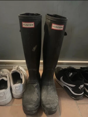 Svarta höga gummistövlar Hunter - Säljer ett par klassiska svarta höga gummistövlar från Hunter. Stövlarna har justerbart spänne på sidan och logotyp framtill. Perfekta för regniga dagar och festivaler. Tillverkade i slitstarkt gummi med tidlös design. NYPRIS 1699kr