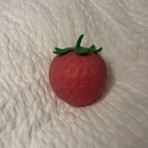 Jordgubbsformad squishy - Rolig squishy i form av en jordgubbe med röd yta och grönt blad på toppen. Tillverkad i mjukt, klämvänligt material som återgår till sin form efter tryck. Perfekt som stressleksak eller dekoration.