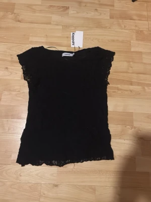 Svart spetsblus från Kappahl - Snygg svart blus från Kappahl med spetsdetaljer och korta ärmar. Blusen har en feminin och elegant look med genombruten spets längs ärmar och nederkant. Perfekt att styla med jeans eller kjol för en trendig outfit.