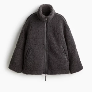 Mörkgrå teddyjacka med dragkedja - Säljer en fluffig mörkgrå teddyjacka med hög krage och hel dragkedja framtill. Jackan har två stora fickor med kant i fejkskinn och en avslappnad passform. Perfekt för dig som vill ha en mysig och trendig look.