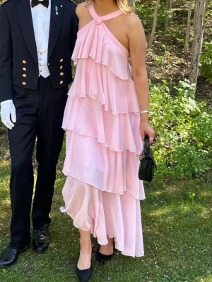 Ljusrosa veromoda klänning - Säljer den populära, slutsålda ljusrosa klänningen med volanger och öppen rygg. Perfekt till sommarens festligheter. Endast använd en gång, så i fint skick. Nypris 1200kr