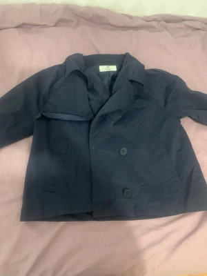 Mörkblå dubbelknäppt rock - Stilren mörkblå rock med dubbelknäppning och bred krage. Klassisk modell med två stora knappar framtill och raka ärmar. Perfekt för dig som vill ha en enkel men snygg look till hösten.