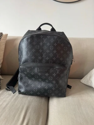 Louis Vuitton svart monogram ryggsäck - Snygg svart ryggsäck från Louis Vuitton i klassiskt monogrammönster. Tillverkad i slitstarkt läder med silverfärgade dragkedjor och detaljer. Rymligt huvudfack och en praktisk ytterficka framtill. Perfekt för dig som vill ha en exklusiv och stilren look.