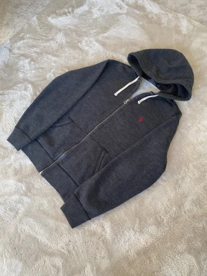 Mörkgrå Ralph Lauren zip-up hoodie  - Mörkgrå zip-up hoodie från Ralph Lauren! skick syns på bilderna, använd men bra skick! Postar inom 24h📦 Köp minst två plagg för 20% rabatt🤝 Tveka inte på att höra av er vid frågor eller funderingar!