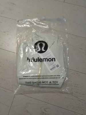 Vit zip-tröja från Lululemon - Snygg vit zip-tröja från Lululemon med hög krage och guldfärgade dragkedjor. Tröjan har figurnära passform, långa ärmar och två fickor framtill. Perfekt för träning eller som ett sportigt lager till vardagslooken.