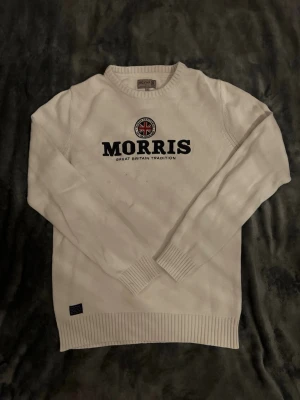 Vit stickad tröja från Morris - Snygg vit stickad tröja från Morris med rund halsringning och svart broderad logga samt Union Jack-detalj på bröstet. Tröjan har ribbade muddar vid ärmslut och nederkant. Perfekt till en clean och klassisk stil. Har några fläckar men är rätt säker på att dom går bort i tvätt m. Pris kan diskuteras vid snabb affär!