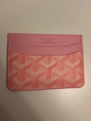 Rosa korthållare - Säljer ett rosa kortfodral med klassiskt mönster i ljusrosa och vitt. Fodralet har flera kortfack och är tillverkat i en kombination av läder och canvas. Perfekt för dig som vill ha en snygg och smidig accessoar i väskan.