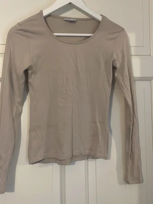 Beige långärmad topp i bomull - En enkel och stilren beige långärmad topp med rund halsringning. Tillverkad i mjuk bomull som känns skön mot huden. Perfekt att matcha med jeans eller kjol för en clean look. Kommer stryckas innan den skickas.