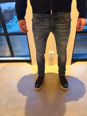 Blå slim fit jeans med tvättade detaljer Jack & Jones - Säljer ett par blå slim fit jeans med snygga tvättade detaljer och klassiska fem fickor. Jeansen har normal midja och smal passform hela vägen ner. Materialet är stretchigt denim som ger en bekväm känsla och följer kroppen. Perfekta för en trendig och avslappnad look. Jack & Jones i storlek 30/32 modellnamn slim/glenn