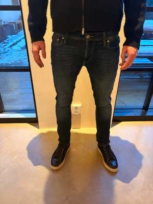 Mörkblå slim fit jeans herr - Säljer ett par mörkblå slim fit jeans med klassisk femficksdesign och normalhög midja. Jeansen har smal passform hela vägen ner och är tillverkade i stretchigt denimtyg för extra komfort. Perfekta för en avslappnad och snygg look. Storlek 30/32 Jack and Jones modellnamn skinny/liam.