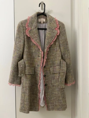 Moiselle HK flerfärgad kappa storlek 36 - En flerfärgad kappa med rosa volangdetaljer längs kragen och ärmsluten. Kappan har en strukturerad väv och en matchande avtagbar bälte i midjan. Den har även två fickor framtill och knäpps med knappar.