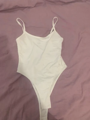 Vit baddräkt med smala axelband - Säljer en enkel och stilren vit baddräkt med smala axelband och hög skärning vid benen. Perfekt för stranden eller poolen. Materialet känns mjukt och stretchigt för en bekväm passform.