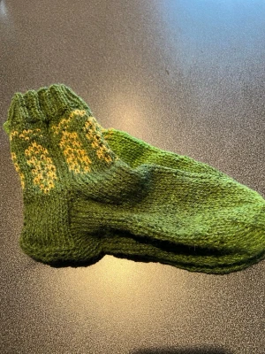 Gröna stickade ullstrumpor lätt milerade, stickade i svensk ull. - Unika gröna stickade strumpor med gult mönster upptill. Perfekta för dig som gillar retrostil och vill ha något varmt och mysigt på fötterna. Handgjorda detaljer och ribbad kant upptill ger extra komfort.