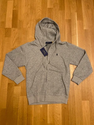 Grå Ralph Lauren Zip-Hoodie - Snygg grå hoodie med dragkedja från Polo Ralph Lauren. Helt nytt skick och storlek M