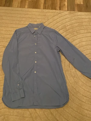Blå skjorta från Burberry London - Snygg blå skjorta från Burberry London med klassisk krage och knappar framtill. Skjortan har lång ärm och är i en tailored passform som ger en clean och stilren look. Perfekt för dig som gillar exklusiva märken och enkel design.