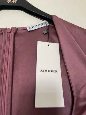 Adore klänning - En klänning från Adore som tyvärr inte passade. Klänningen är i storlek 40 men jag skulle säga att den är liten i storleken. Den har en fin urringning och sitter figurnära. Den har även lite större och puffiga ärmar vilket gör den till en fin cocktailklänning. Klänningen har även en fin vinröd/lila färg. Klänningen har aldrig använts och är helt ny.