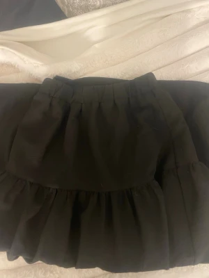 Svart volangkjol med resårmidja - Säljer en svart kortkjol med volang och resår i midjan. Kjolen har en luftig och flowy känsla, perfekt för att styla med en crop top eller stickad tröja.