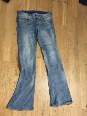 Blå bootcut jeans från Cheap Monday - Säljer ett par ljusblå bootcut jeans från Cheap Monday med klassisk femficksdesign och slitna detaljer. Jeansen har låg midja och är tillverkade i denim med en snygg tvättad look. Perfekta för en avslappnad och trendig stil.