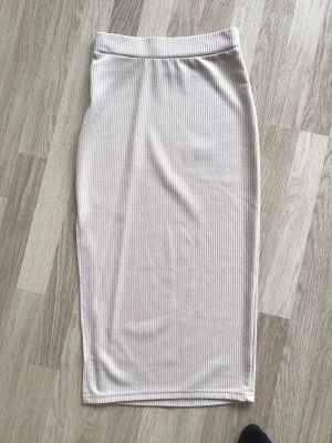 Beige ribbad kjol i midilängd från Boture, stl XS - Snygg beige tight midikjol med ribbad struktur och rak passform. Kjolen har en enkel och stilren design och snygg slits på ena nedre sidan. Sparsamt använd så i mycket gott skick. Passar perfekt till många olika outfits. Från Boture, stl XS.